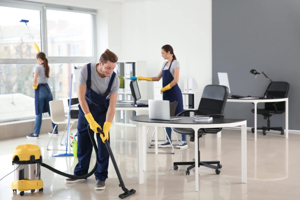 A group of individuals diligently clean and organize a bustling office space centered around a black and white computer desk.
