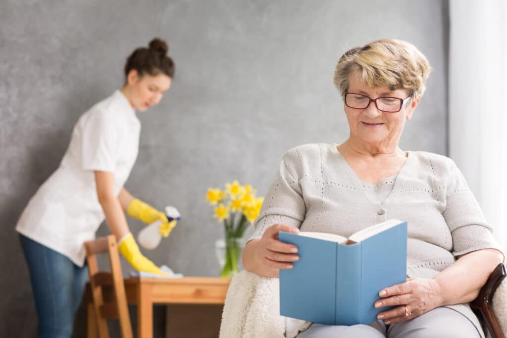 A woman immersed in a book sits in a cozy chair. She cleans a wooden table. An older woman with glasses smiles warmly. A baby in a white tee shirt captures innocence. Coffee adds warmth to the serene scene.